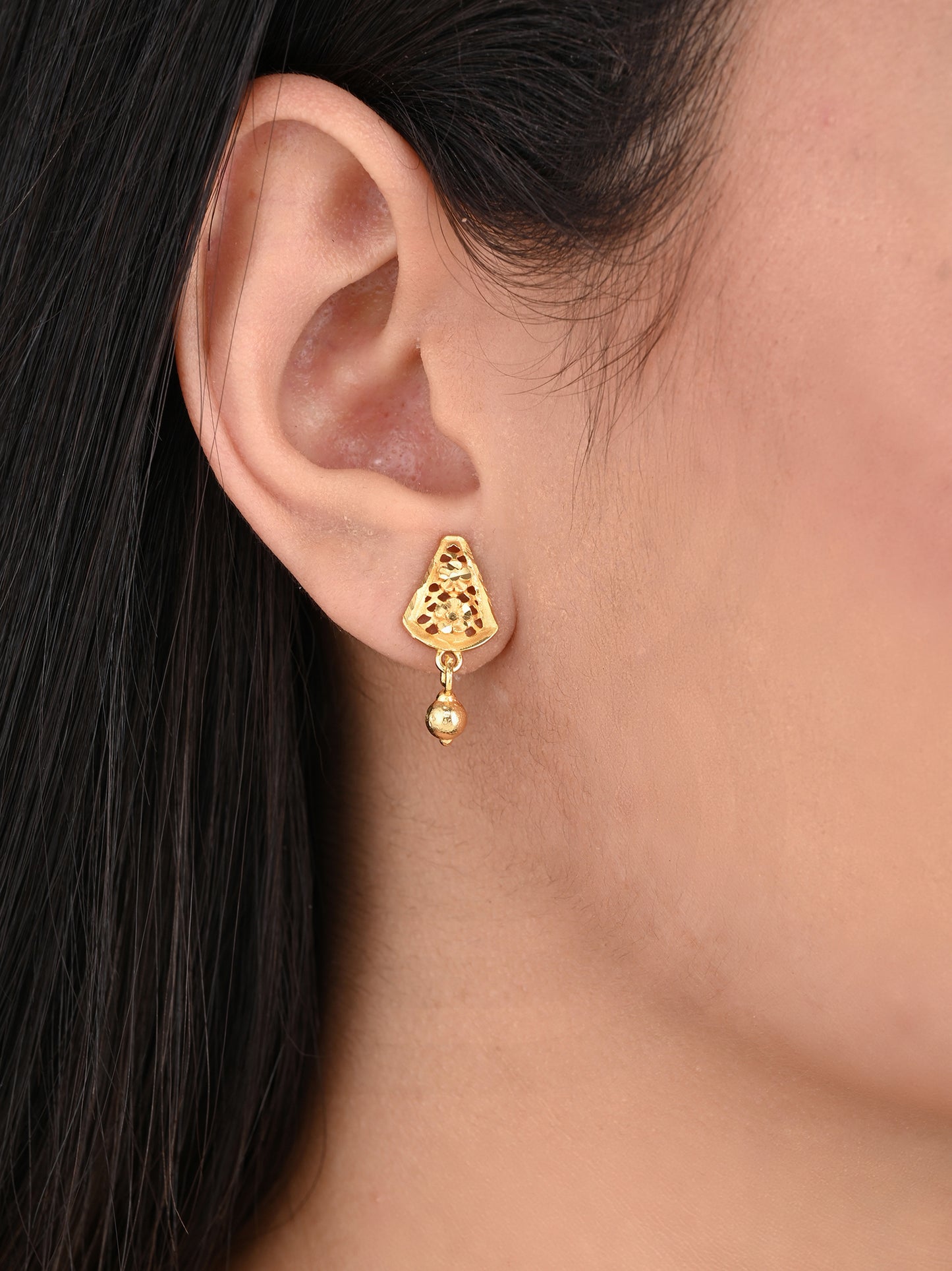 Gold earring worn by a person with dark hair